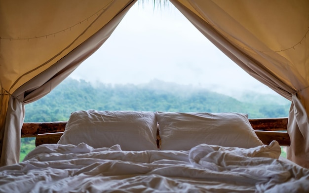 外の霧の日に美しい自然の景色を望むテントの中にある白い居心地の良いベッド
