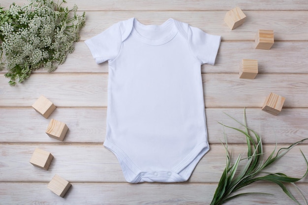 Foto mockup di tutina a maniche corte in cotone bianco con fiori bianchi di erba verde e blocchi di giocattoli per bambini design modello di tuta di genere neutro modello neonato pagliaccetto stampa presentazione mock up