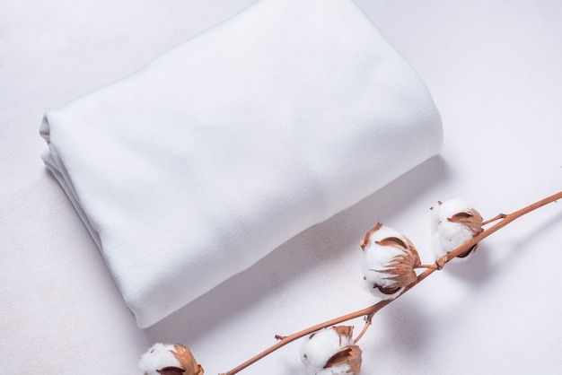 White cotton fabric with cotton flower branch on wooden background