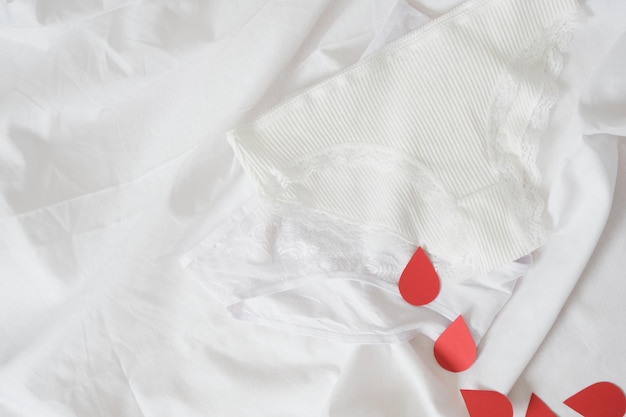 Белые хлопковые женские трусики с красными бумажными каплями, похожими на красную кровь. Концепция менструации, половое воспитание, открытый разговор о менструации у женщин, без табу, без стыда
