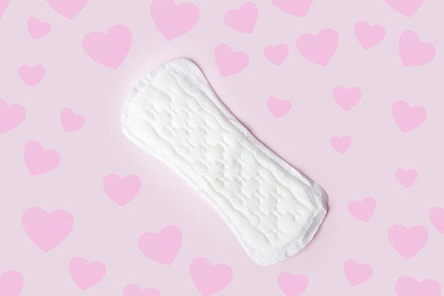 White cotton sanitary napkin sanitary pad on a pastel pink background with pink hearts as drops top view flat lay minimalism Menstrual cycle Women's hygiene and health care
