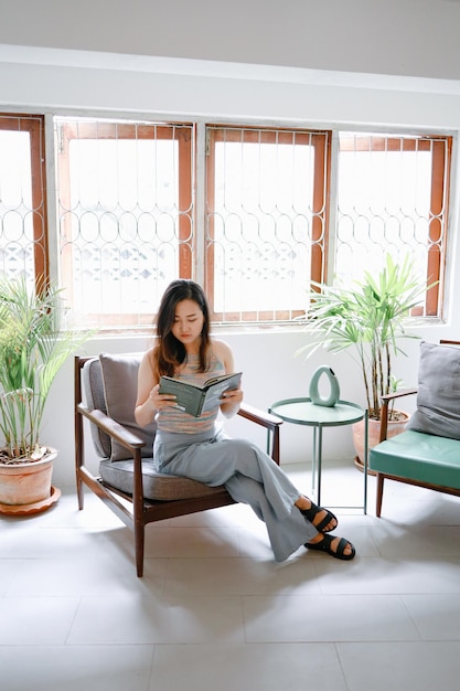 Белая уютная домашняя азиатка расслабляется, читая книгу дома и успокаиваясь