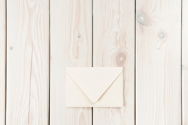 白い木の板の背景に敷設の白いクラフト手作りの閉じた紙の封筒 レトロなスタイルの送信メッセージ モックアップ