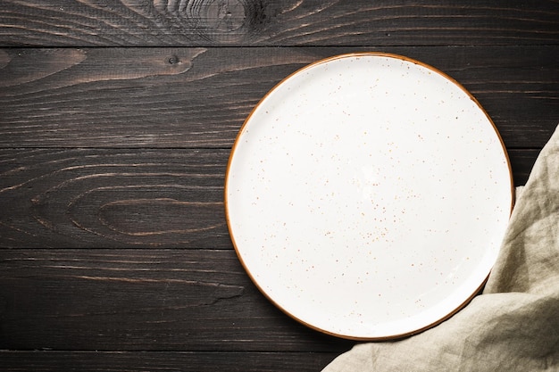 Фото Белая тарелка на темном деревянном столе изображение сверху с местом для копирования