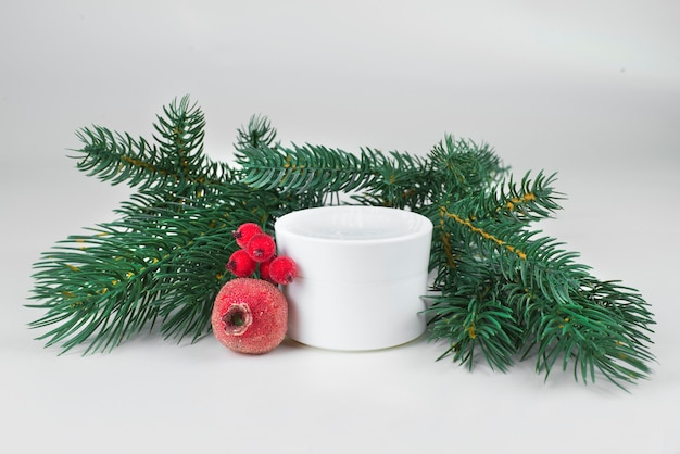 white cream jar with christmas tree branches and red christmas things on a light background