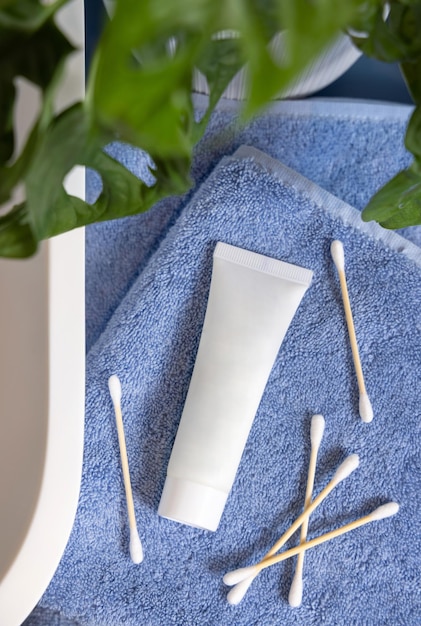 White cream tube on blue towels near basin and green monstera in bath lid mockup