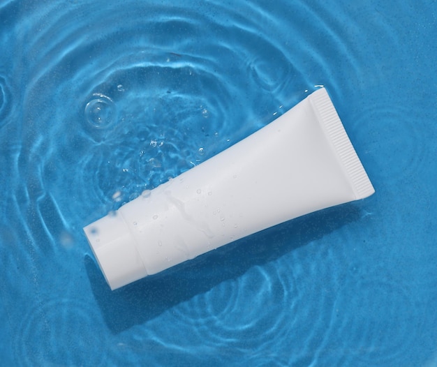 white cream tube in blue water with shadows beauty concept top view
