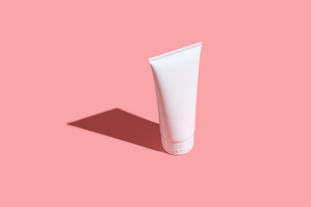 White cream tube on light pink table. Care about face, hands, legs and body skin.