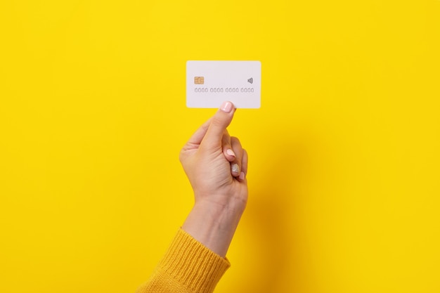 White credit card in female hand, card with electronic chip over yellow background