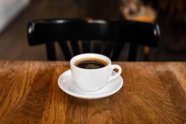 Foto una tazza bianca di caffè nero su un piatto sul tavolo di legno in un caffè