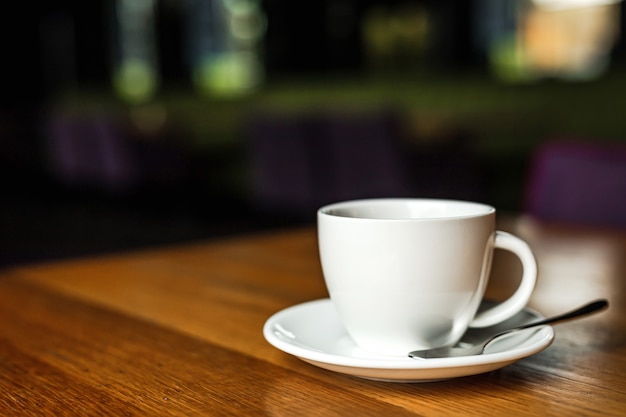 A white cup of black coffee, white saucer, spoon, wooden table, at a cafe