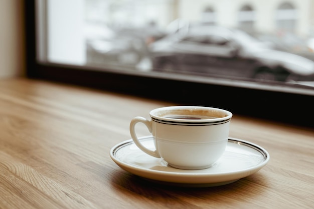 A white cup of black coffee on a wooden windowwill