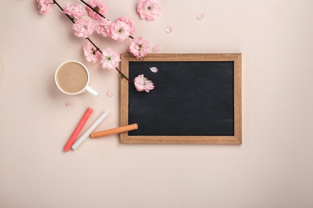 Cappuccino tazza bianca con fiori di sakura, lavagna su uno sfondo rosa pastello