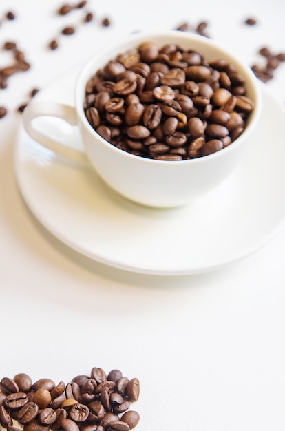 White cup and coffee beans on a white background. Selective focus.