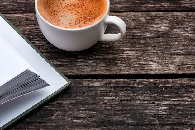 Tazza di caffè bianco e un libro sul tavolo di legno