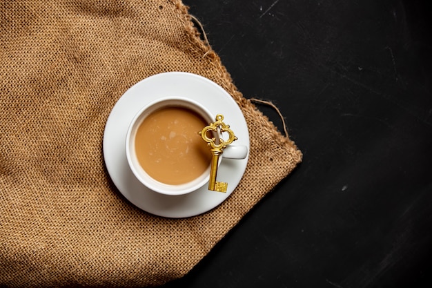 White cup of coffee and golden key on dark background