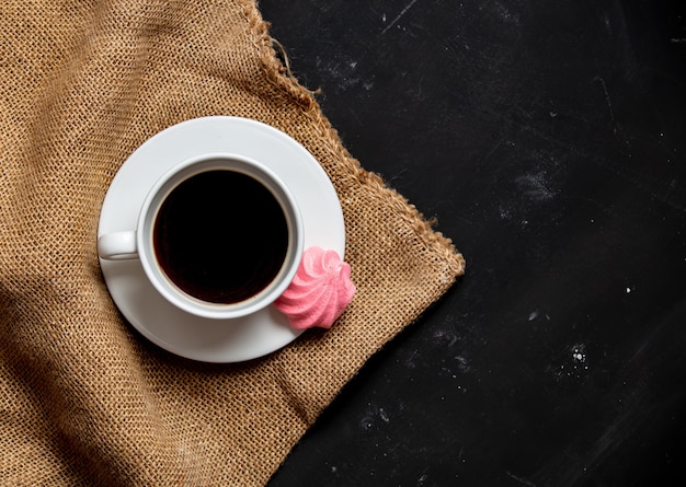 White cup of coffee and meringue on dark background