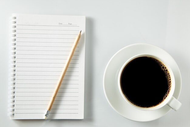 White cup of coffee morning on wooden table with notebook