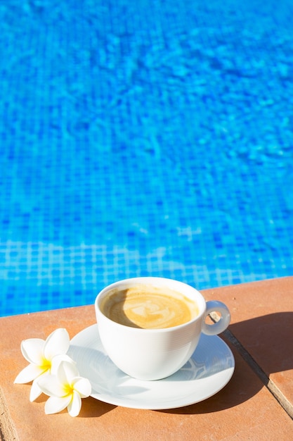 White cup of coffee near pool blue water