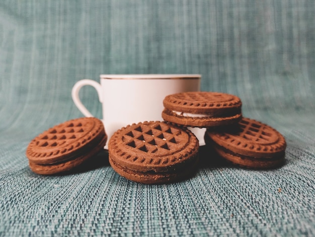 Tazza di caffè bianca e biscotti marroni rotondi su sfondo blu