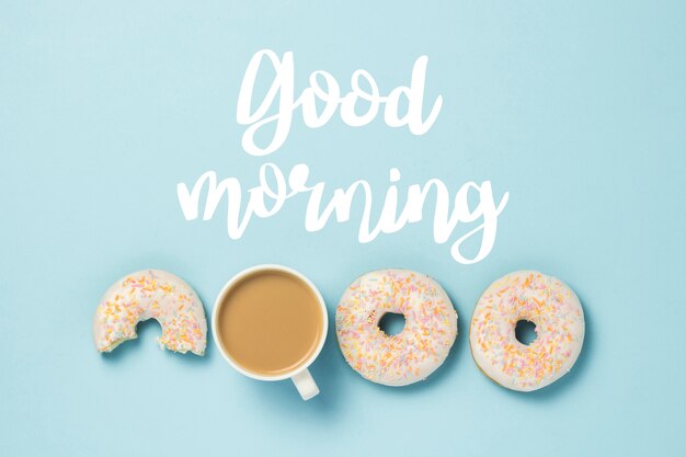 Photo white cup, coffee or tea with milk and fresh tasty donuts on a blue. added text good morning. bakery concept, fresh pastries, delicious breakfast, fast food. flat lay, top view.