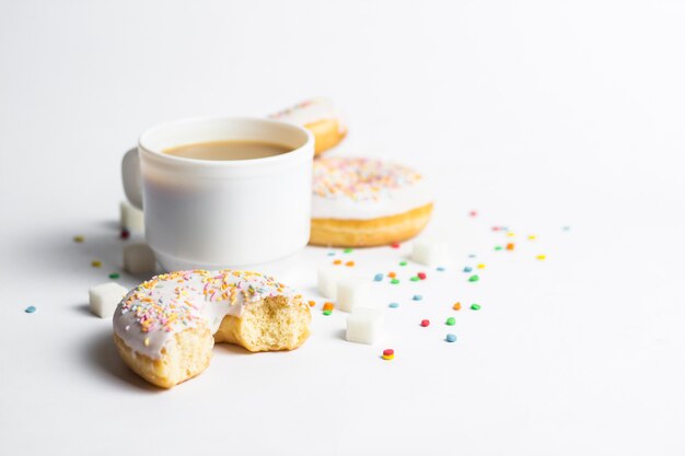 White Cup, coffee or tea with milk and fresh tasty donuts, sweet multicolored decorative candy on a white background. Bakery concept, fresh pastries, delicious breakfast, fast food.