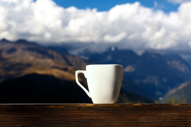 White cup of coffee and tea with steam on wood table over mountains landscape