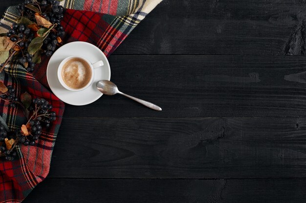 White cup of the coffee and vintage scarf on black wooden background