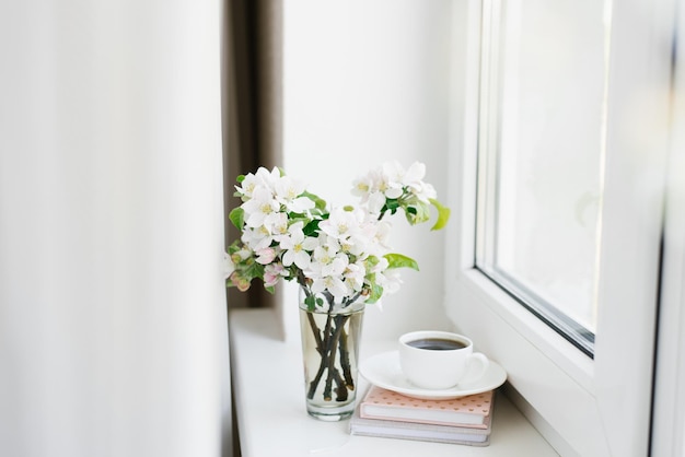 白い皿に白いコーヒー カップの本と窓辺に花瓶の花 居心地の良いイースター春の静物