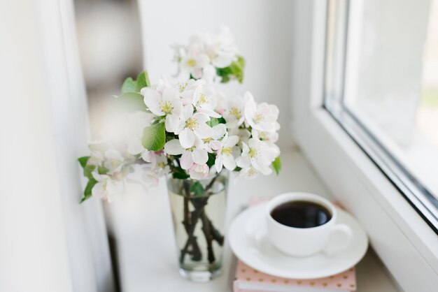 白い皿に白いコーヒー カップの本と窓辺に花瓶の花 居心地の良いイースター春の静物