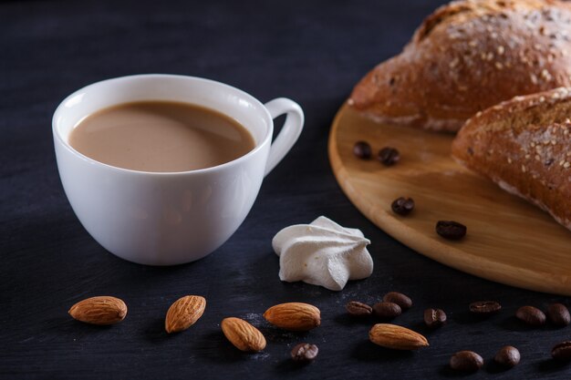 クリームと黒の背景にパンとコーヒーの白いカップ