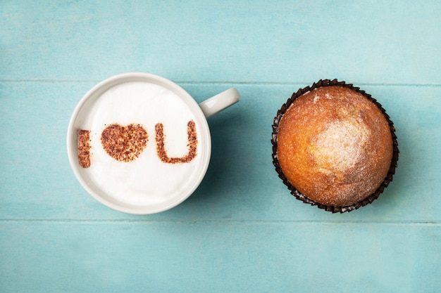 White cup of coffee with the inscription on the foam i love you and a cupcake.