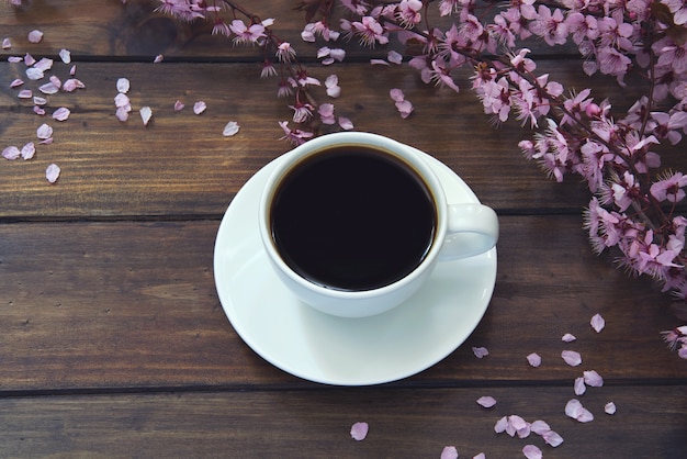  white Cup of coffee on wooden tale and beautiful pink flowers