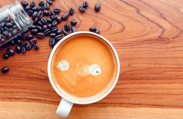 White cup of espresso coffee and Roasted coffee beans on a wooden background