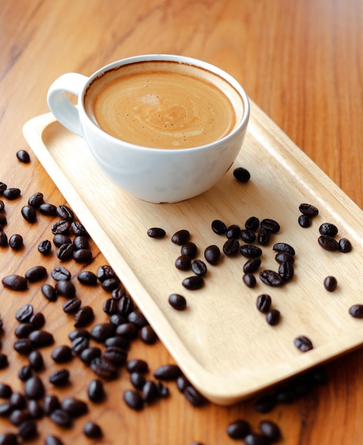 Белая чашка кофе эспрессо и жареные кофейные зерна на деревянной стойке в кофейне