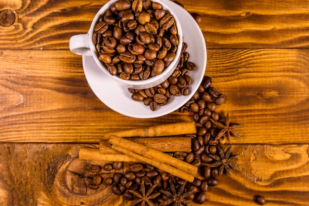 White cup filled with coffee beans star anise and cinnamon sticks on rustic wooden table Top view