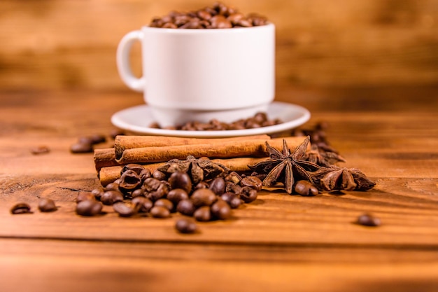 White cup filled with coffee beans, star anise and cinnamon sticks on rustic wooden table