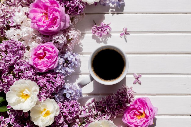 White cup of fresh balck coffee on wooden white table with purple lilac branch morning routine coffe