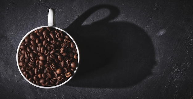 White cup of freshly brewed roasted coffee beans on gray background