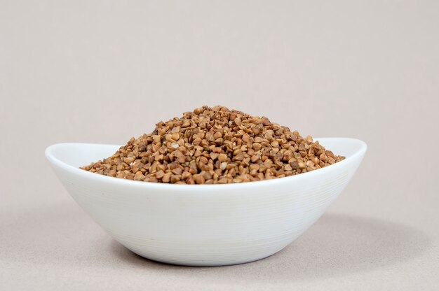 White cup full of buckwheat on a gray background side view