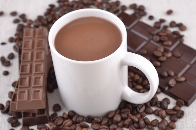 Белая чашка горячего шоколада на кофейных зернах и шоколадном фоне