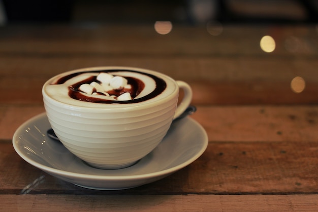 a white cup of hot chocolate topping with marshmallow on wood table