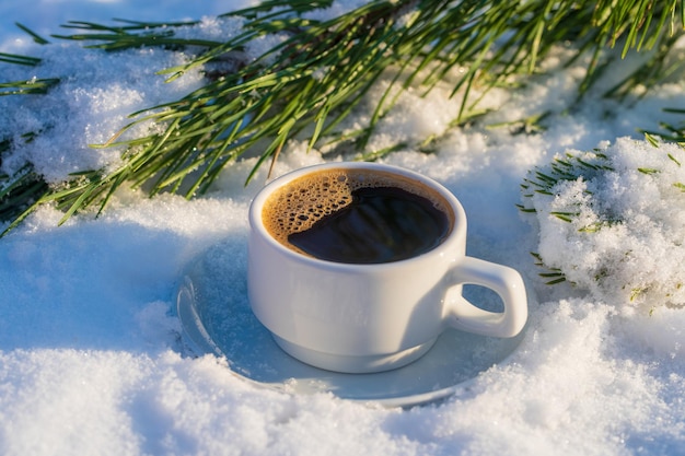 White cup of hot coffee on a bed of snow and white background close up