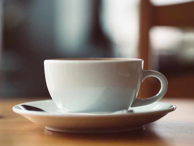 White cup of hot coffee served on wooden table in the cafe.