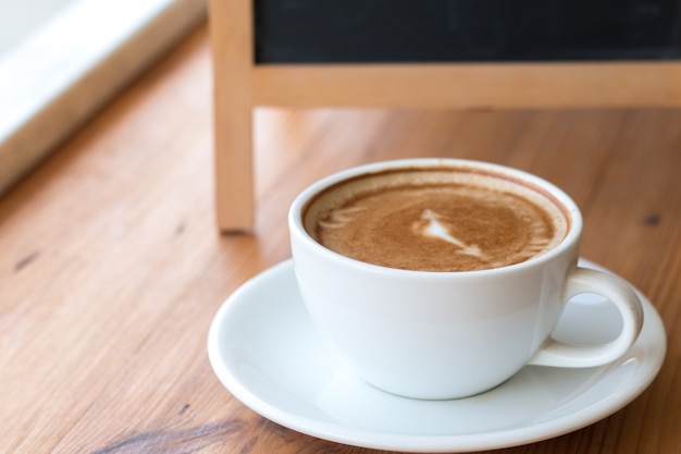 木製のテーブルに白いコーヒーの白いカップ、喫茶店での書き込みメニューのための空のブラックボードとの休憩のリラックスタイムでの仕事時間やリフレッシュメント前のリフレッシュメント