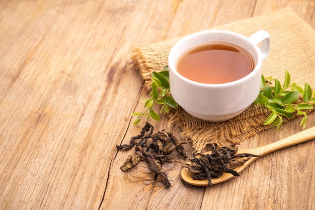 White cup of hot tea and dry tea leaf on wooden table