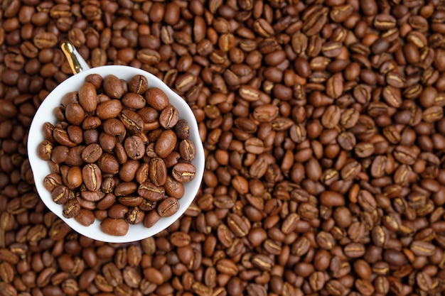 A white cup is peppered with beans against the background of coffee beans.