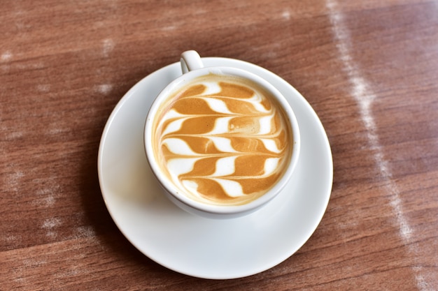 white cup of latte coffee on wooden table. subject is blurred.