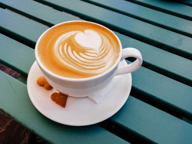 Tazza bianca di latte con arte su legno verde. schiuma artistica, tazze in ceramica bianca