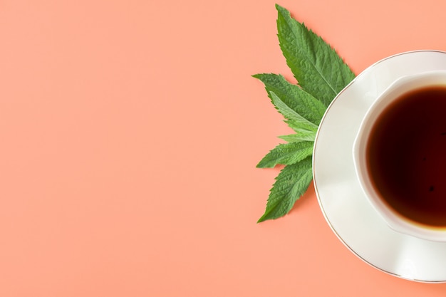 Белая чашка чая и блюдце с листьями мяты на ярком фоне. черный чай с мятой. вид сверху.